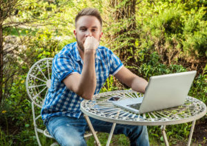 Handsome young working with computer at an iron table in the garden.