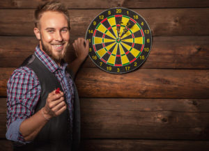 Portrait of young friendly man against old wooden wall with darts game