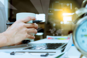 Business woman with alarm clock working on laptop and holding a cup of coffee