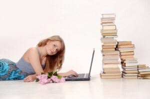 Woman with a laptop next to a pile of books