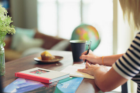 Woman writing in a notebook with globe and cup of coffee in the background